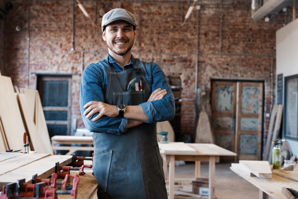 Young joiner work at his workstation. Successful handsome businessman with stylish cap work in carpentry